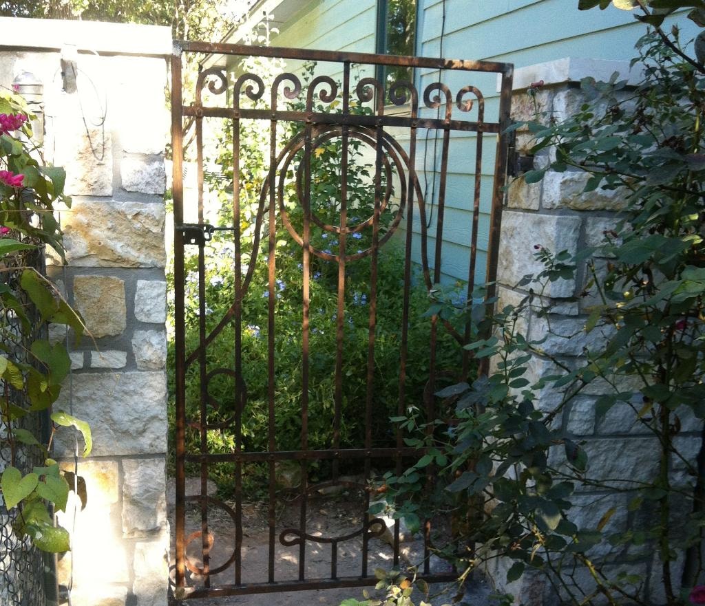 Ornate iron garden gate with stone pillars and climbing roses